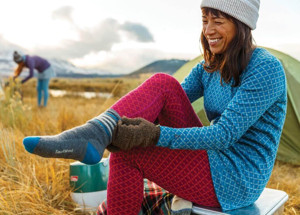Frau zieht sich Wandersocken an unter freiem Himmel
