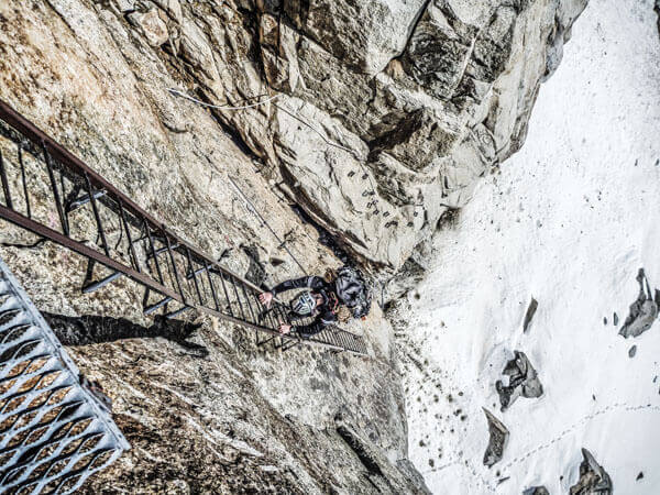 Klettersteiggänger auf einer Leiter hoch an der Bergwand.