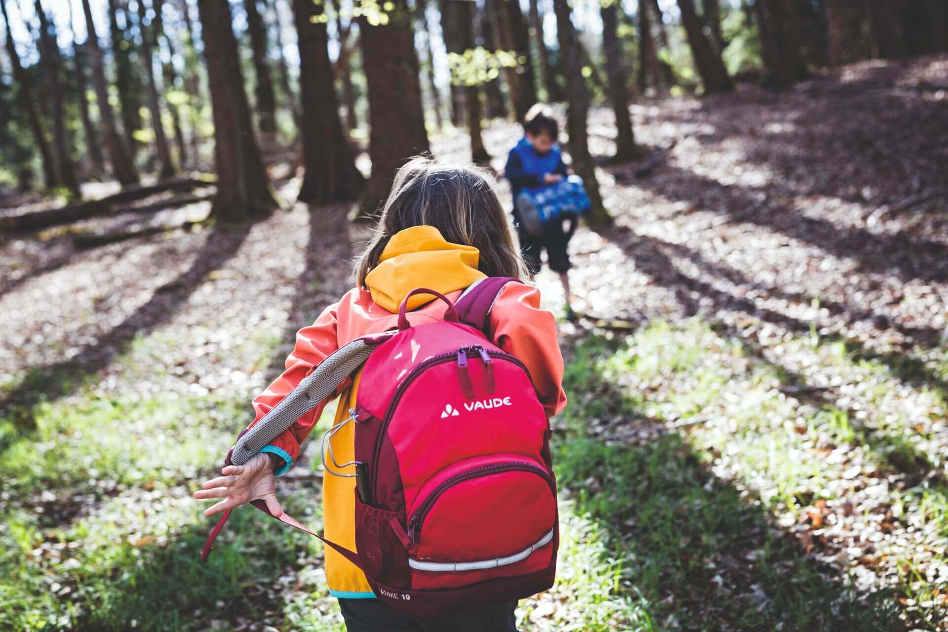 Zwei Kinder laufen durch den Wald mit Rucksäcken