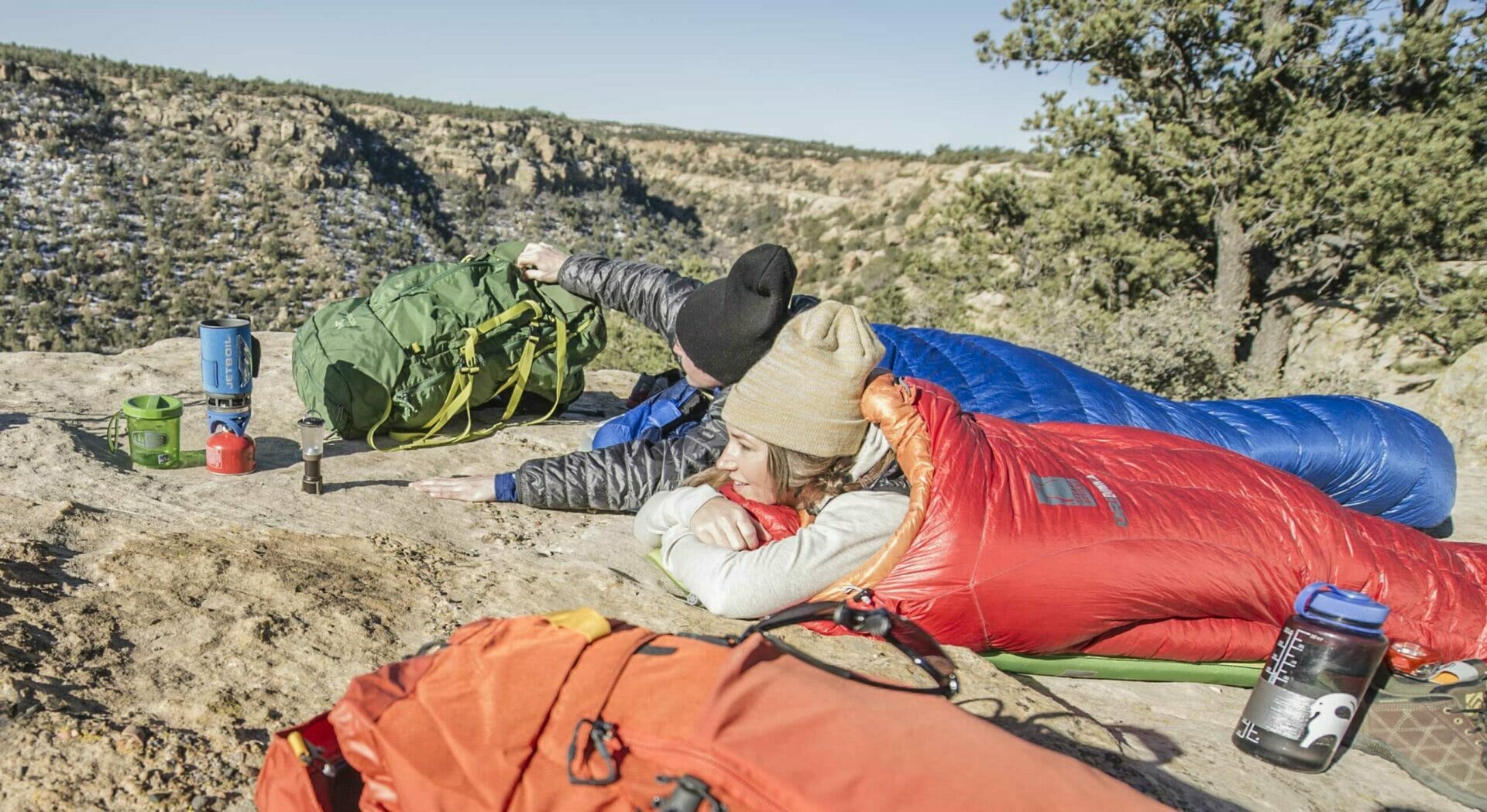 Zwei Camper in einer Steppe im Schlafsack mit Isomatte als Unterlage auf Stein.