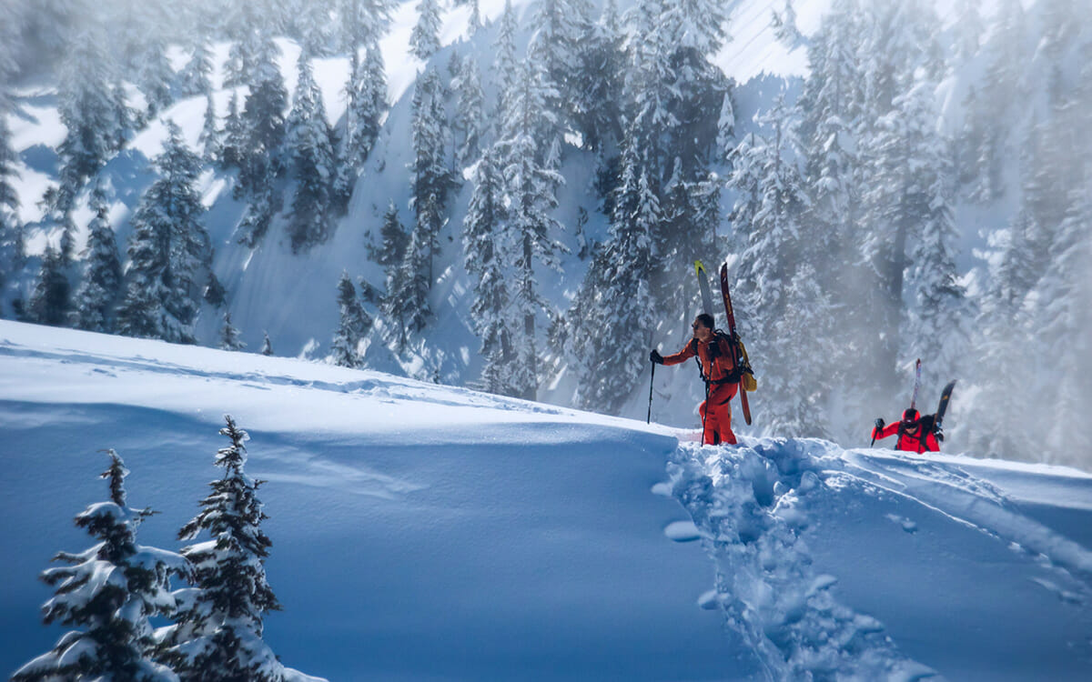 Zwei Skitourengeher mit den Ski auf dem Rücken an einem Steilen Aufstieg.