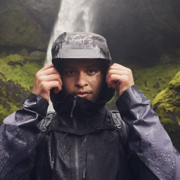 Mann mit Regenjacke steht vor einem Wasserfall