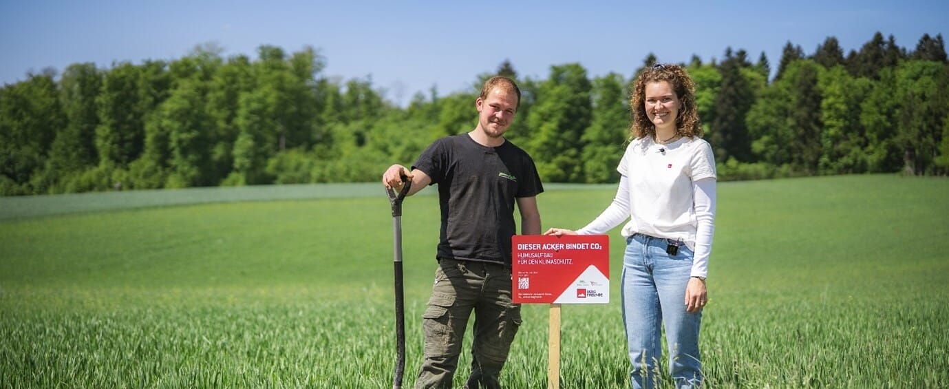Zwei Menschen stehen im Feld vor einem Schild