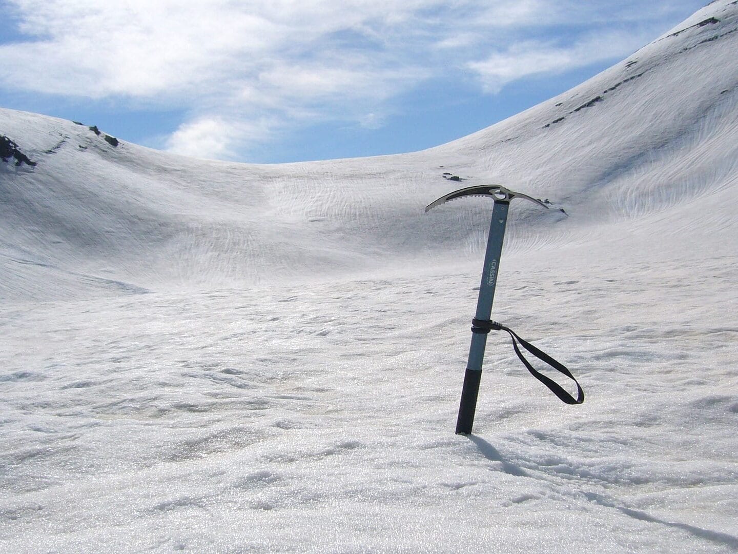 Eispickel im Eis mit schneebedeckten Bergen im Hintergrund