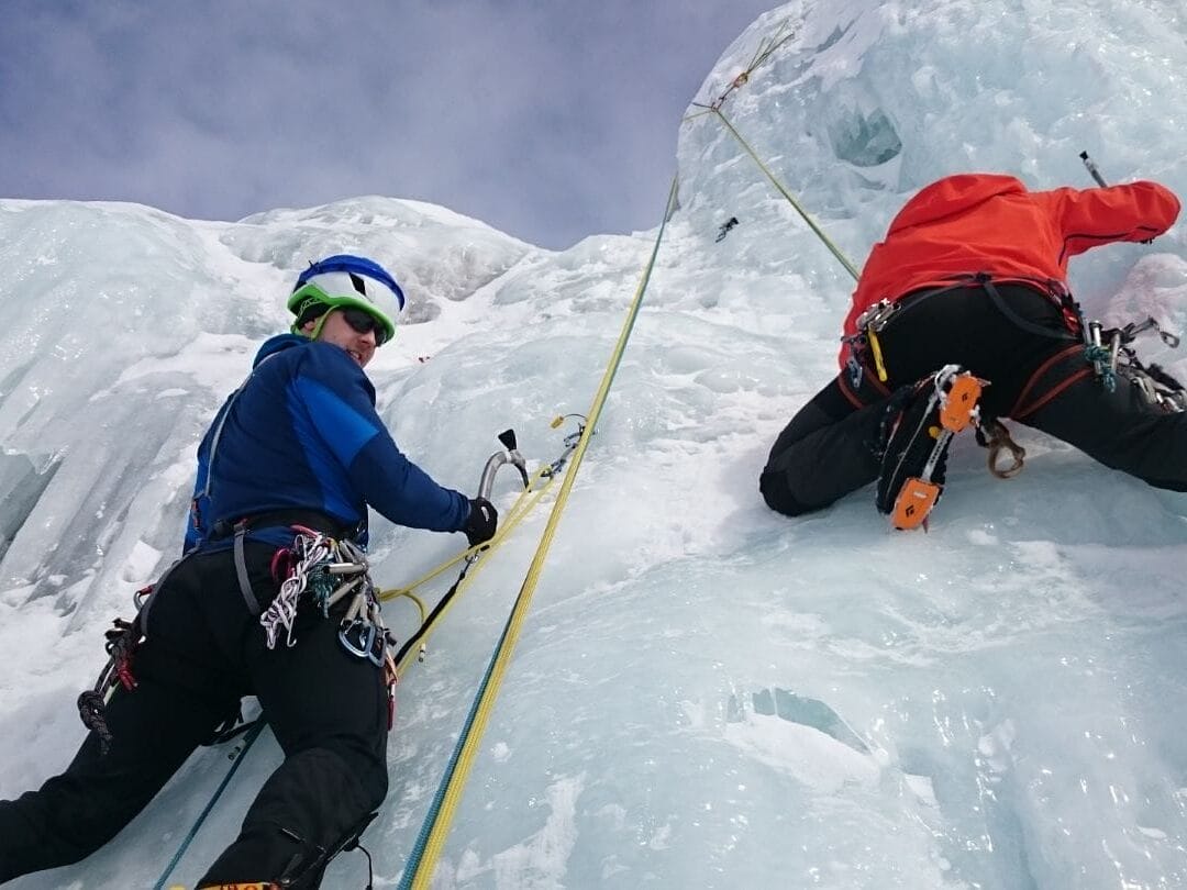Zwei Kletterer mit Eispickel und Sicherung, die eine Eiswand beklimmen