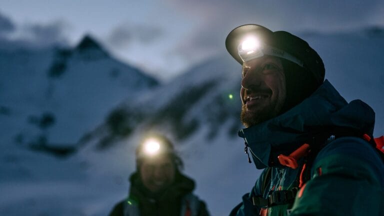 Zwei Menschen mit aufgesetzten Stirnlampen in einer verschneiten Bergwelt
