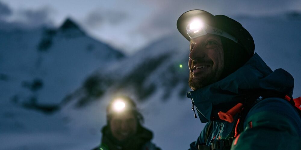 Zwei Menschen mit aufgesetzten Stirnlampen in einer verschneiten Bergwelt