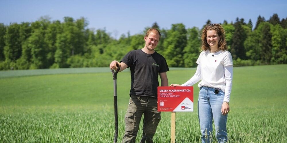 Zwei Menschen stehen im Feld vor einem Schild