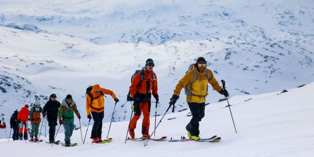 Eine Schlange an Menschen geht mit Skiern an den Füßen einen Berg hoch