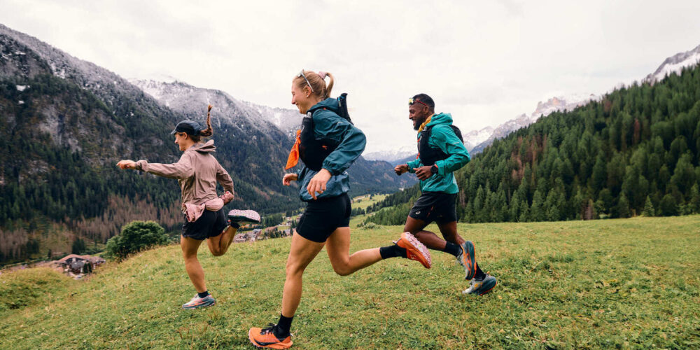 Drei Trailrunner rennen über eine Wiese